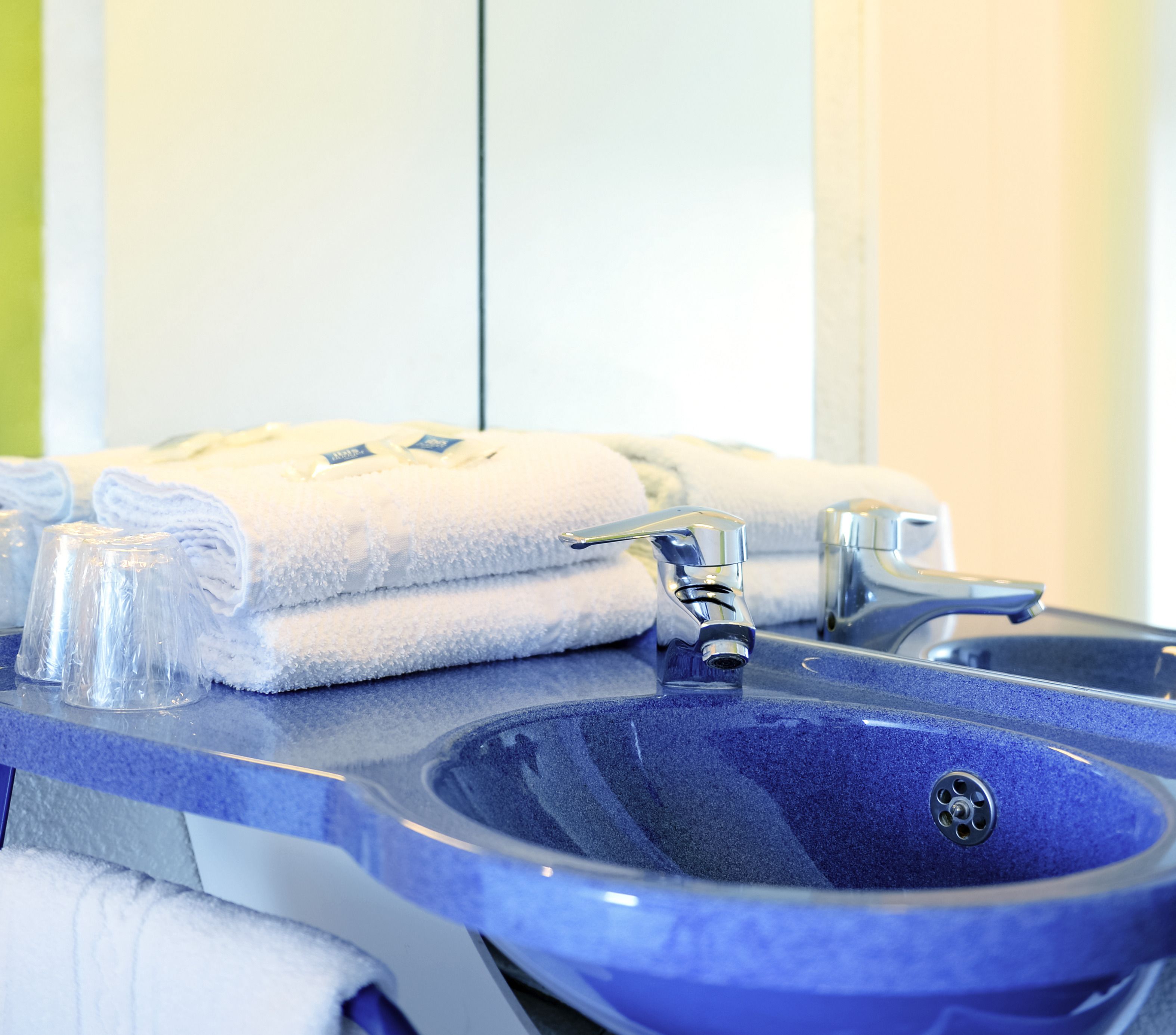 A bathroom with a blue sink, two faucets, and a towel rack with folded towels.