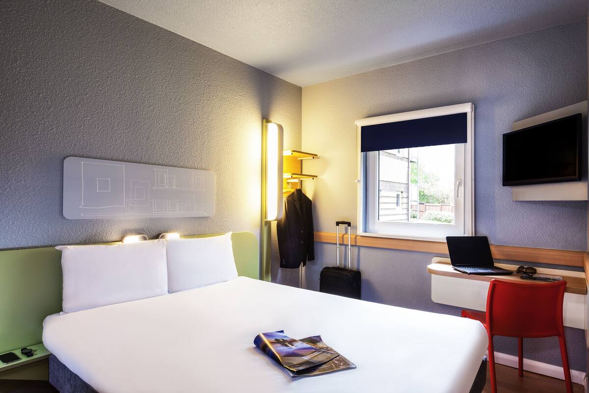 Habitación de hotel con cama, escritorio con una laptop, silla, televisor y ventana con vistas.