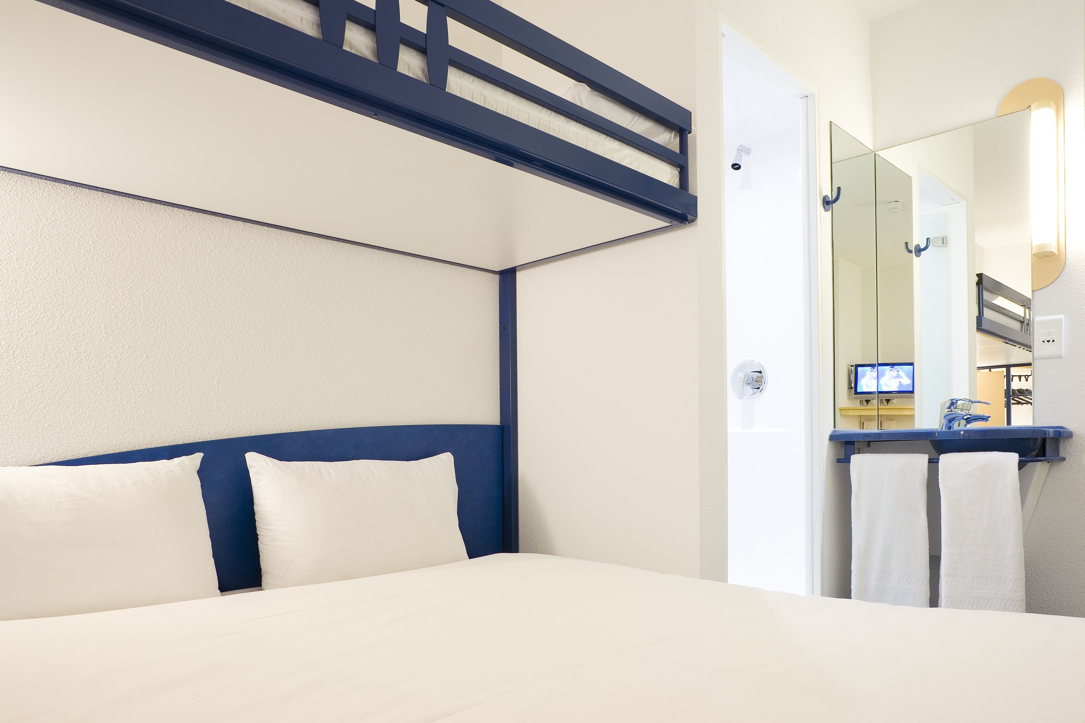 A hotel room with a bed, a TV, and a bathroom with a mirror and towel rack.