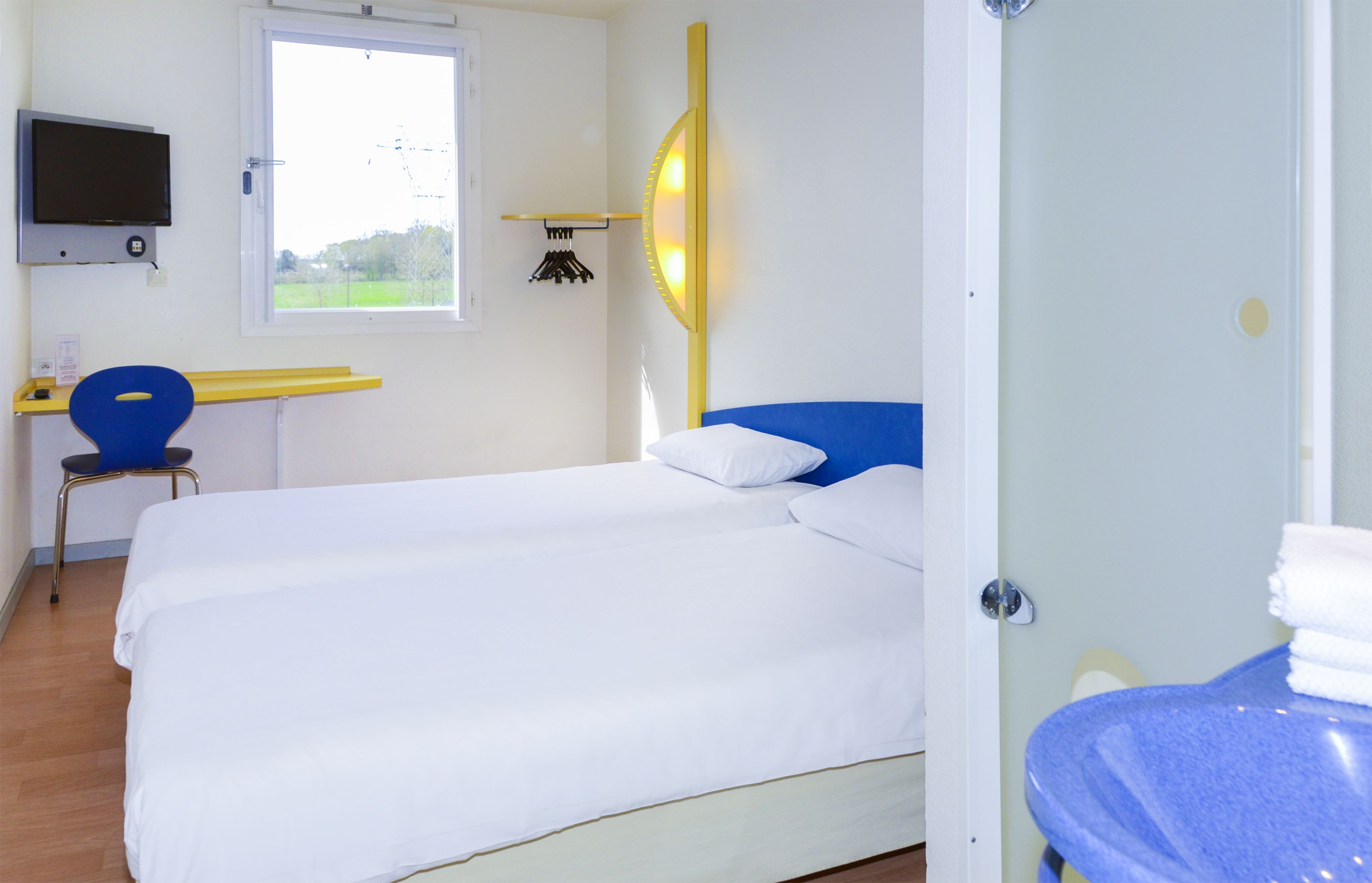 Hotelkamer met twee bedden, een bureau met stoel, een televisie en een raam met uitzicht op groen.