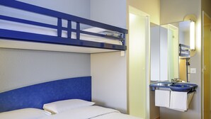 Una cama litera con ropa de cama blanca, un baño con lavamanos y espejo azules, y una toalla colgada en la pared.