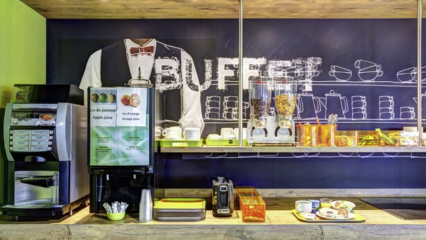 Un mostrador de buffet con una máquina de café, un panel de menú y diferentes alimentos exhibidos.