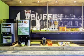 Un mostrador de buffet con una máquina de café, un panel de menú y diferentes alimentos exhibidos.