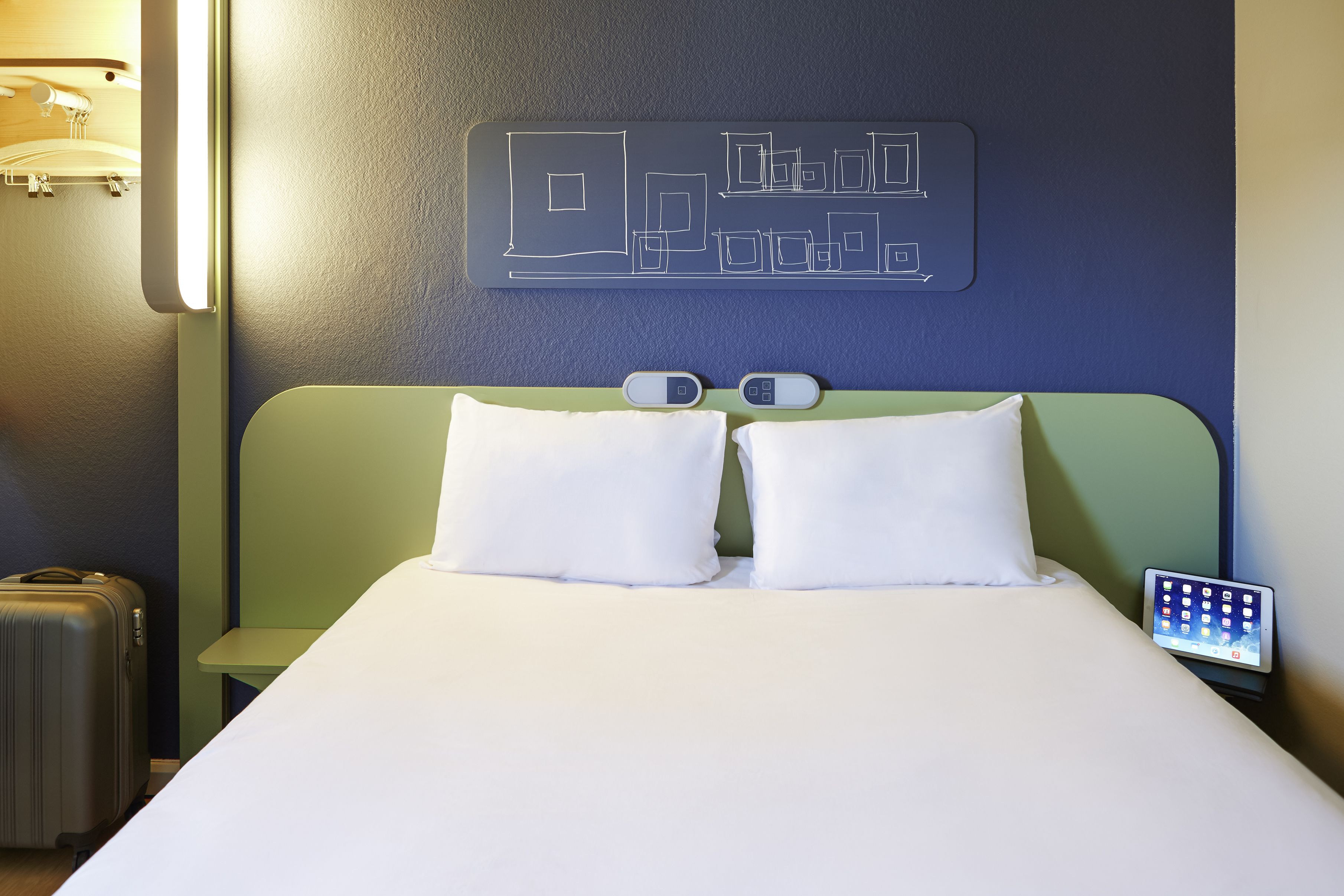 A neatly made bed with white bedding, a green headboard, and a bedside table with a lamp and a digital clock.