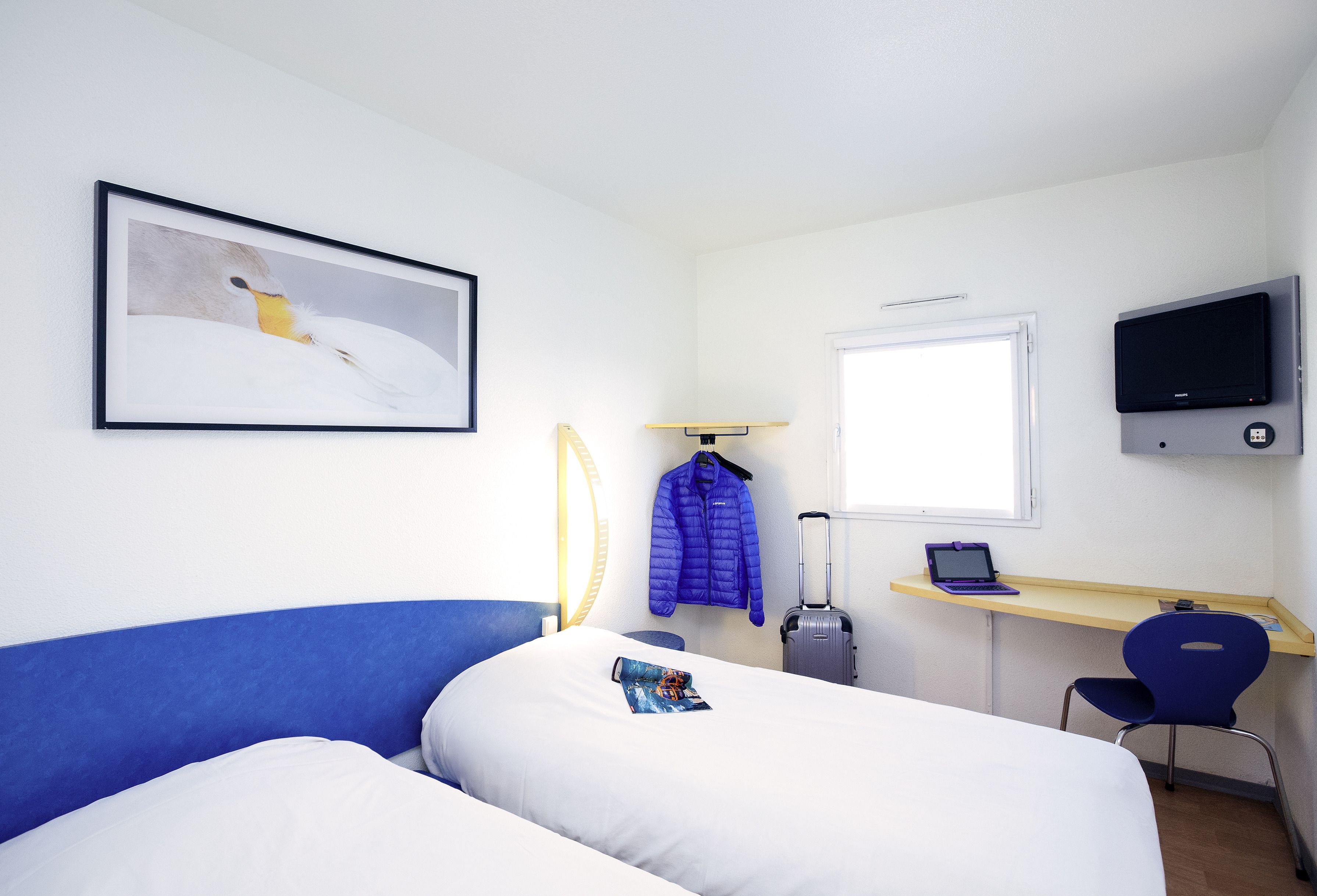 A hotel room with a bed, a desk with a laptop, a chair, a TV, and a coat rack.
