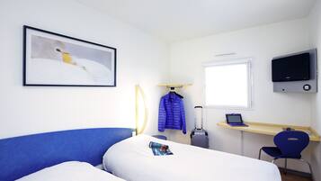 A hotel room with a bed, a desk with a laptop, a chair, a TV, and a coat rack.