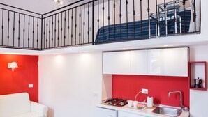 A compact kitchen with a gas stove, sink, and white cabinets. A red accent wall and a white sofa are also visible. - B&B Mergellina (Naples)
