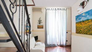 A hotel room with a wooden floor, a white sofa, a painting of a field, and a window with a curtain. - B&B Mergellina (Naples)