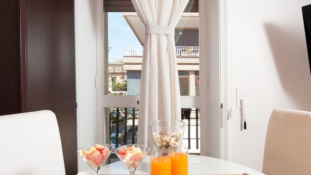 A breakfast tray with pastries, fruits, and beverages on a table by a window with a view of buildings. - Mirage (Lecce)