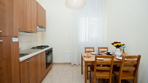 A compact kitchen with wooden cabinets, a gas stove, and a dining table set for two with chairs. - Mirage (Lecce)