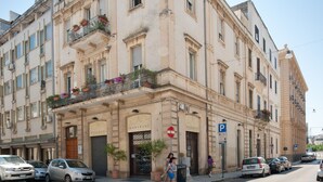 A corner building with a ground-floor entrance, multiple windows, and balconies with flower boxes. - Mirage (Lecce)