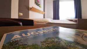 A hotel room with a bed, a desk, and a magazine on the table. - Hotel Jakoberhof (Augsburg)