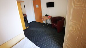 A hotel room with a bed, a desk with a chair, a television mounted on the wall, and a door. - Hotel Jakoberhof (Augsburg)