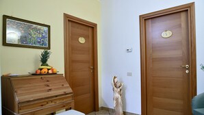 A room with two wooden doors, a wooden dresser with fruit on top, a statue, and a framed picture on the wall.