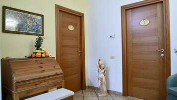 Una stanza con due porte in legno, un comò di legno con della frutta sopra, una statua e un quadro appeso al muro.