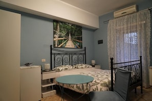 A bedroom with a bed, a bedside table, a chair, a small table, and a painting on the wall. - Le 4 Meraviglie (Rome)