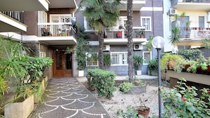 A multi-story residential building with balconies, potted plants, and a paved pathway.