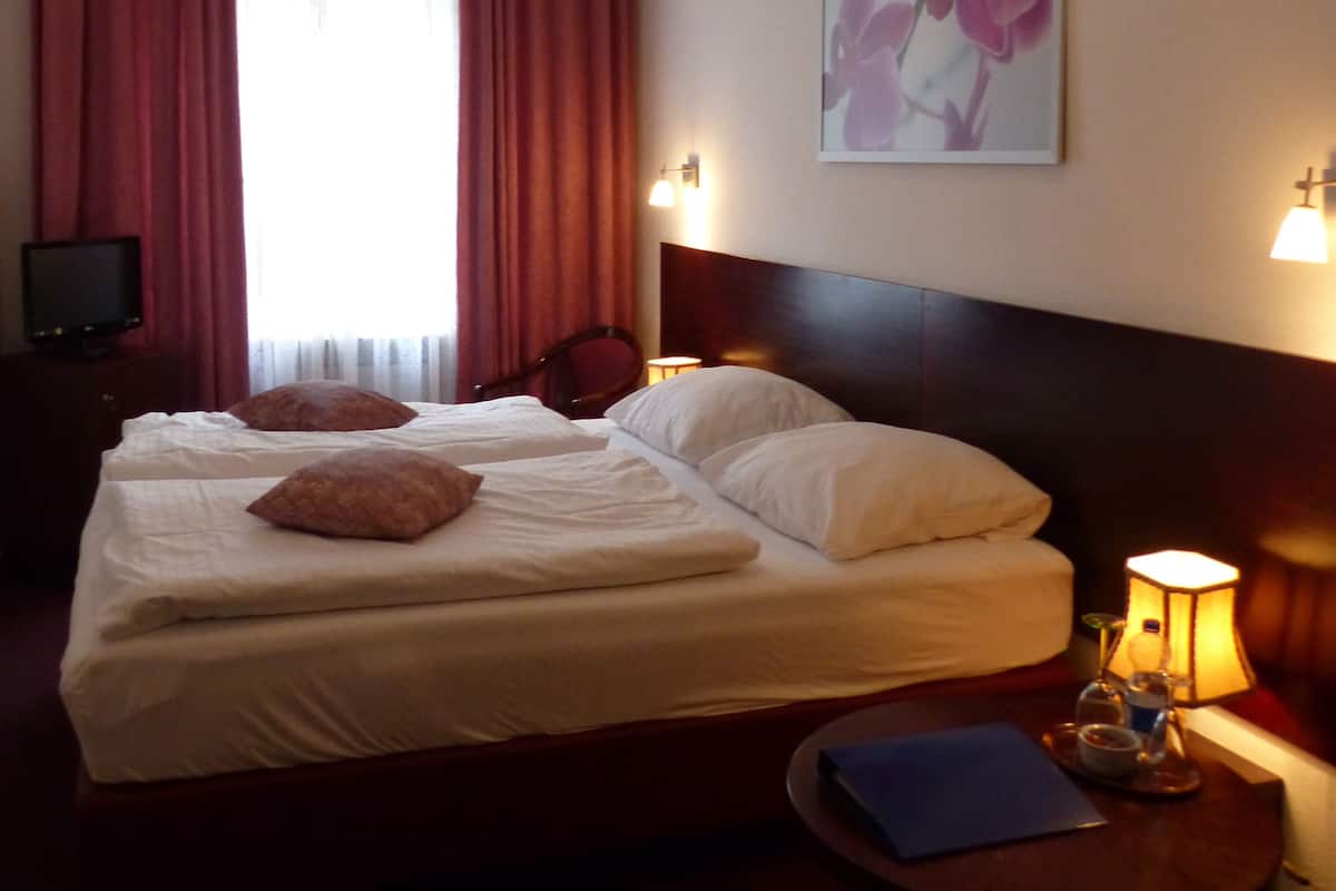 A hotel room with two beds, a desk, a lamp, and a painting on the wall.