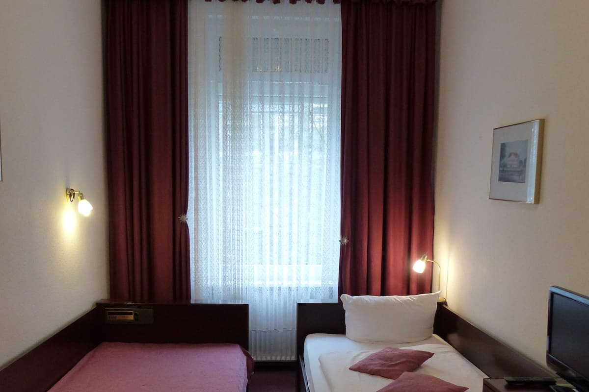 A hotel room with two single beds, a TV, and a window with curtains.