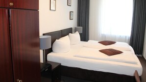 A hotel room with a large bed, a nightstand, a lamp, and a wardrobe. - Hotel Novalis (Berlin)