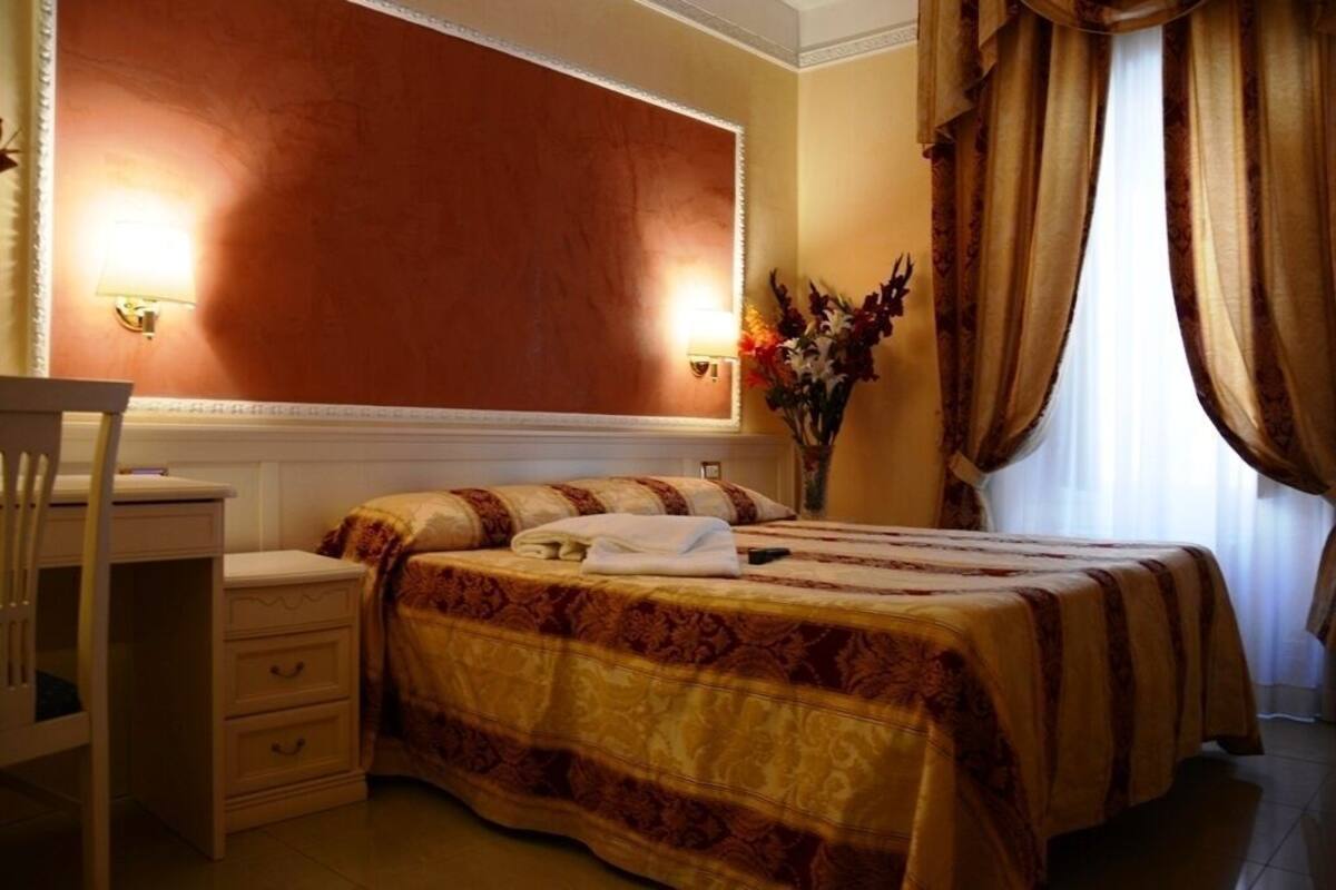 Une chambre d’hôtel avec un lit, une table de chevet, une lampe et des rideaux.