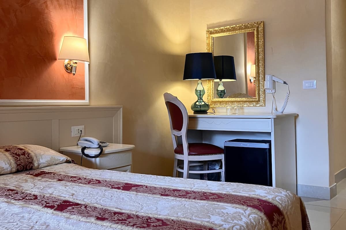Une chambre d’hôtel équipée d’un lit, d’un bureau, d’une chaise, d’un miroir, d’une lampe, d’un téléphone et d’un sèche-cheveux.