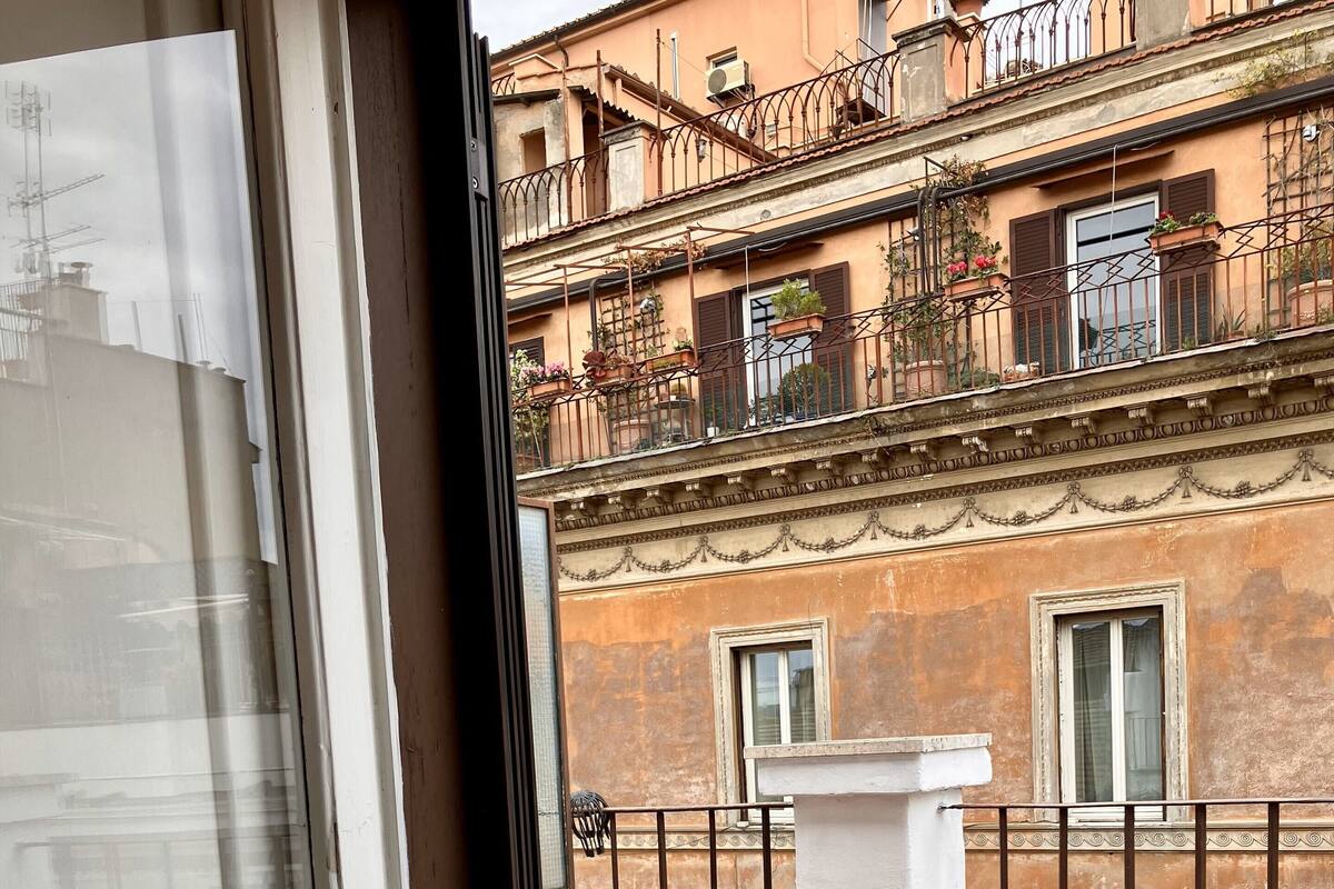 Un balcon avec une table et deux chaises rouges, donnant sur un immeuble doté de balcons et de fenêtres.