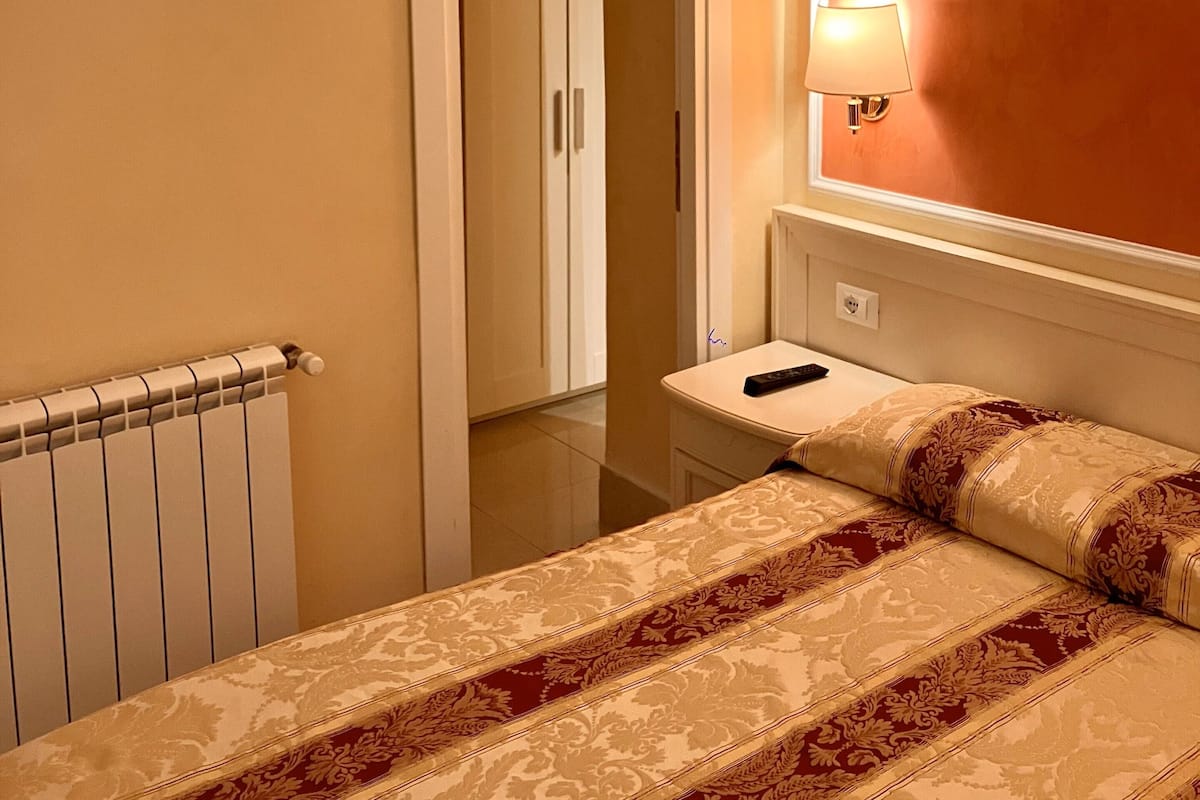 Une chambre d’hôtel avec un lit, une table de chevet, une lampe et un radiateur.