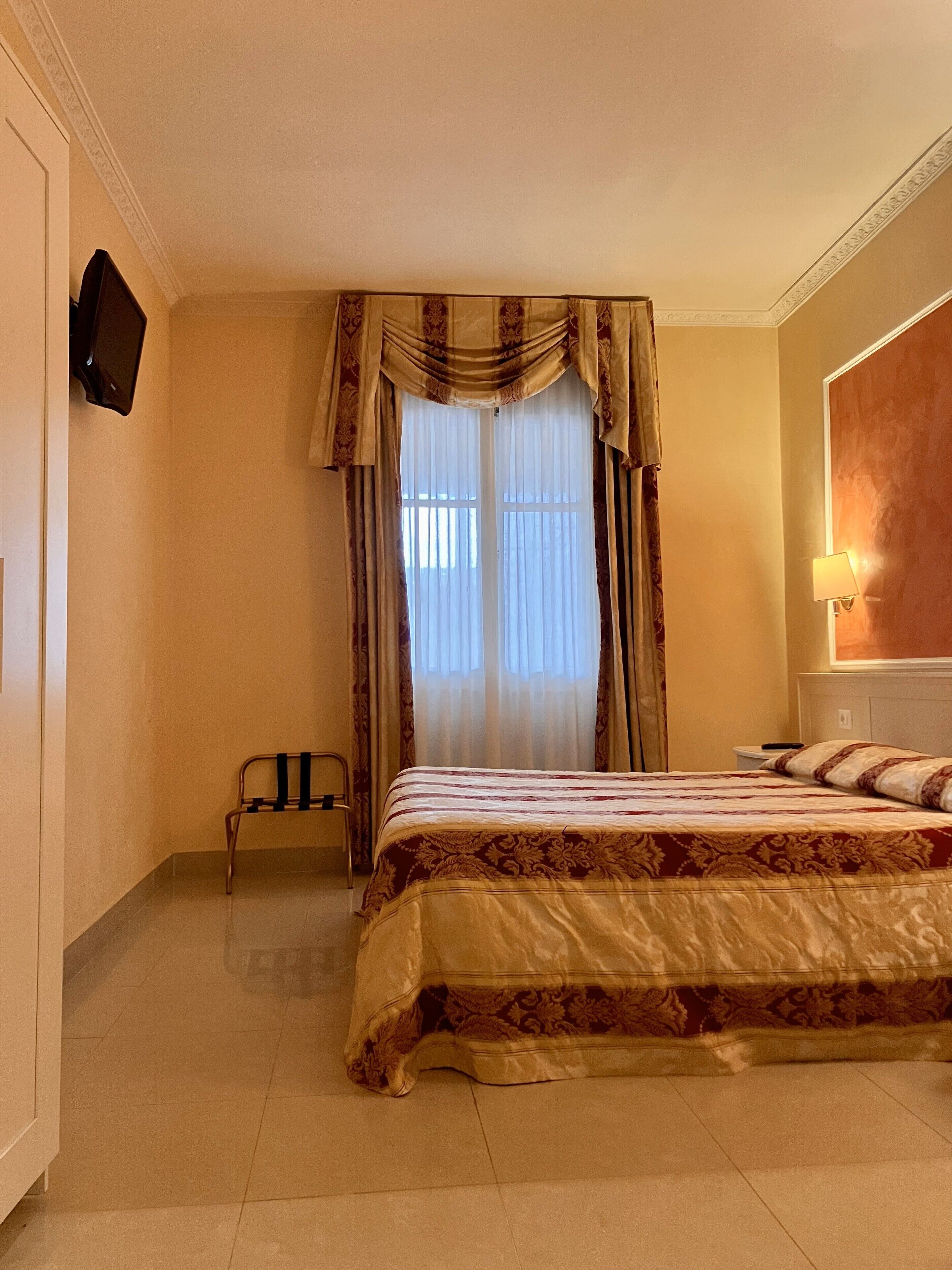 Une chambre d’hôtel avec un grand lit, une chaise, un téléviseur fixé au mur et une fenêtre avec des rideaux.