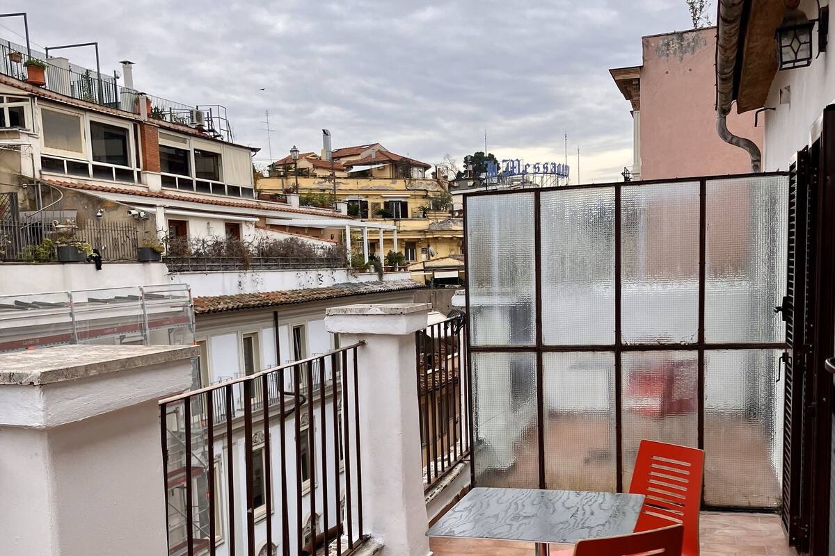 Un balcon avec une table et des chaises, une vue sur le paysage urbain et une balustrade blanche.