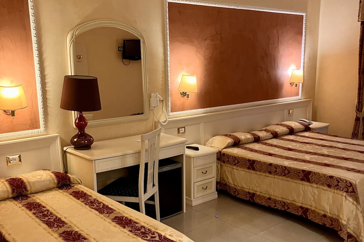 Une chambre d’hôtel avec deux lits, un bureau, une chaise, un miroir et des lampes de chevet.