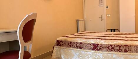 A hotel room with a bed, a desk, a chair, a television, and a door.