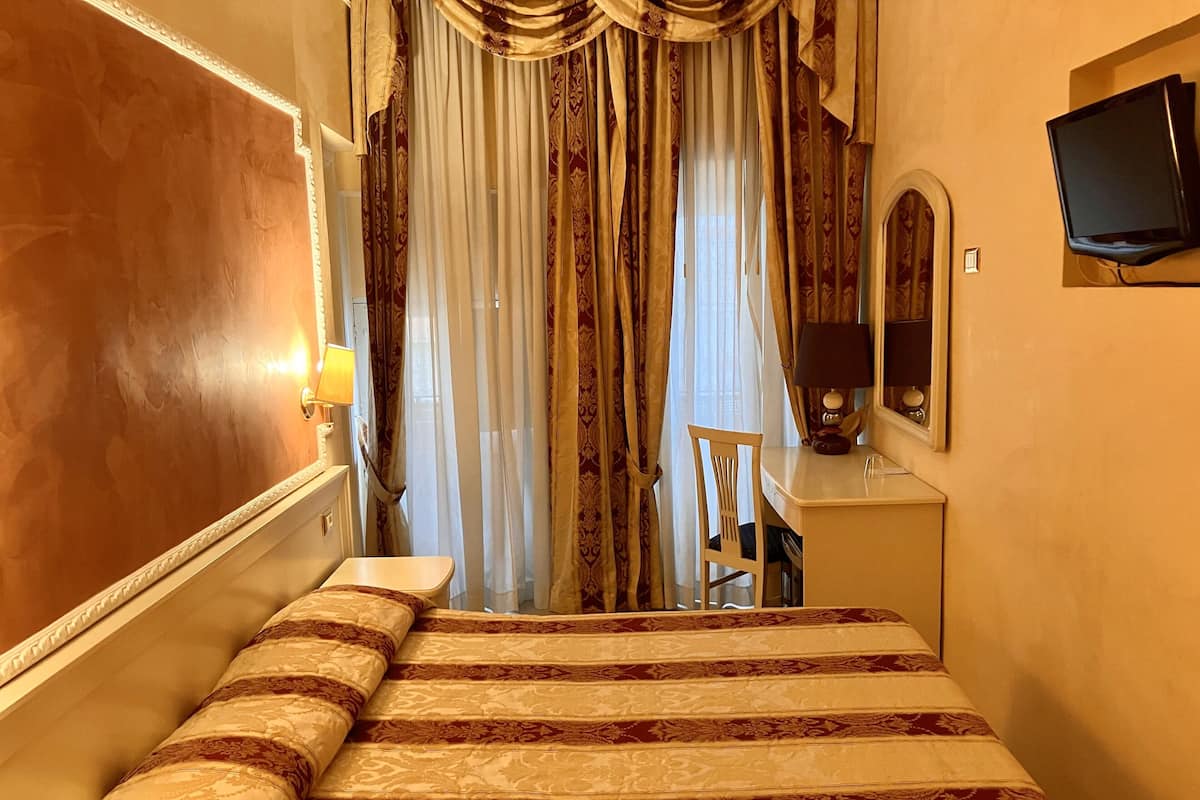 Une chambre d’hôtel avec un lit, un bureau, une chaise, une télévision et des rideaux.