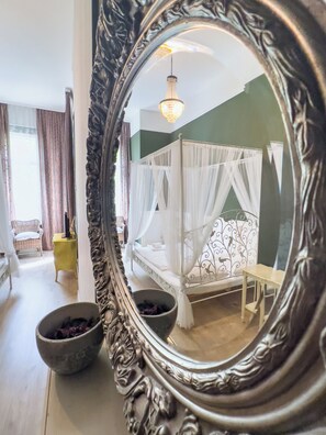 Une chambre à coucher avec un lit à baldaquin, un grand miroir décoratif et une vue sur le paysage urbain par la fenêtre.