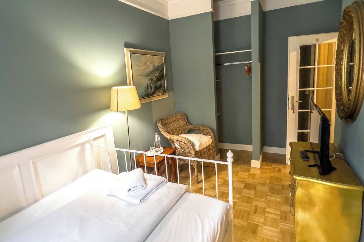 Ein Schlafzimmer mit Bett, Sessel, Lampe, Schminktisch und einer Tür zu einem anderen Raum.