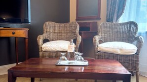 A living room with a wooden coffee table, two wicker chairs, a television, and a mirror. - Hotel Maison Am Olivaer Platz (Berlin)