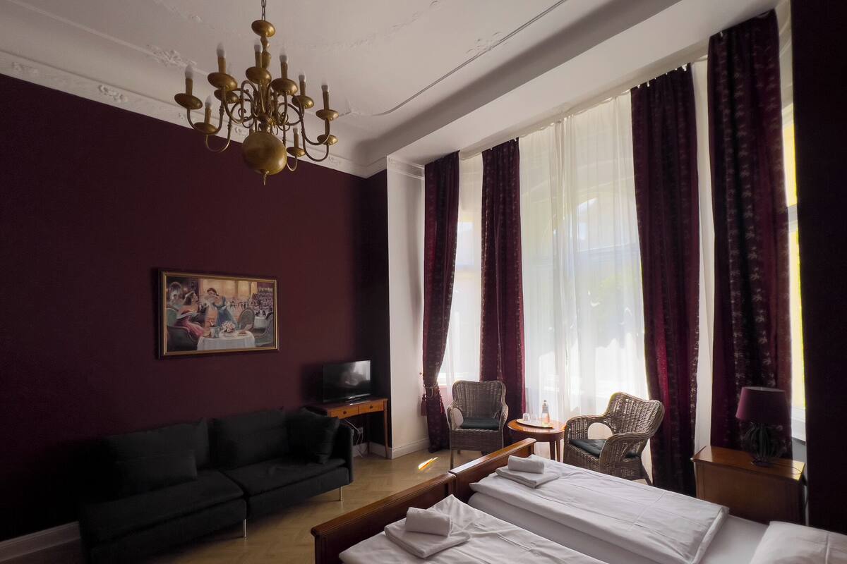 Ein Hotelzimmer mit einem Bett, einer Couch, einem Fernseher, einer Chandelieber und einem Gemälde an der Wand.