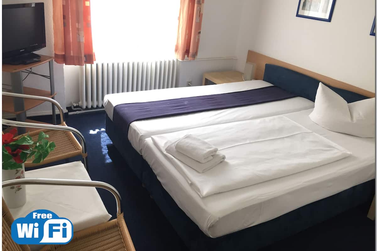 A hotel room with a bed, a chair, a small table, a TV, and a radiator.