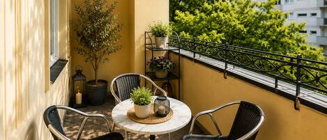 A balcony with a round table, two chairs, potted plants, and a railing.