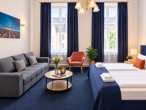 A hotel room with a sofa, a chair, a bed, a round table, and a window with curtains. - Hotel Seifert Berlin am Kurfürstendamm (Berlin)