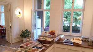 Un bufé de desayuno con diversos alimentos, una planta en maceta y una ventana con vista a follaje.