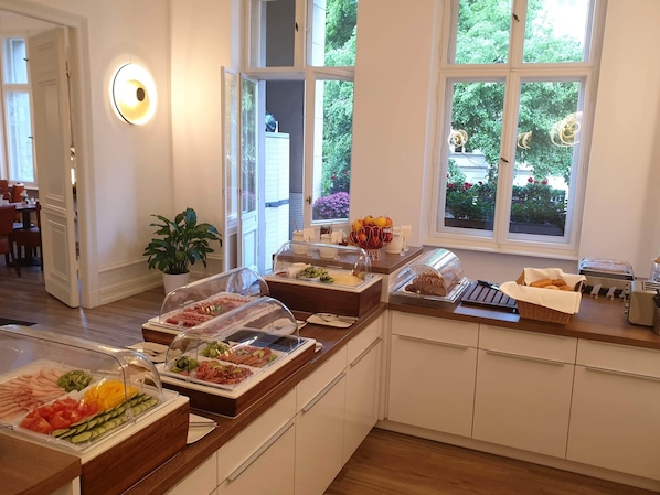 Un bufé de desayuno con diversos alimentos, una planta en maceta y una ventana con vista a follaje.
