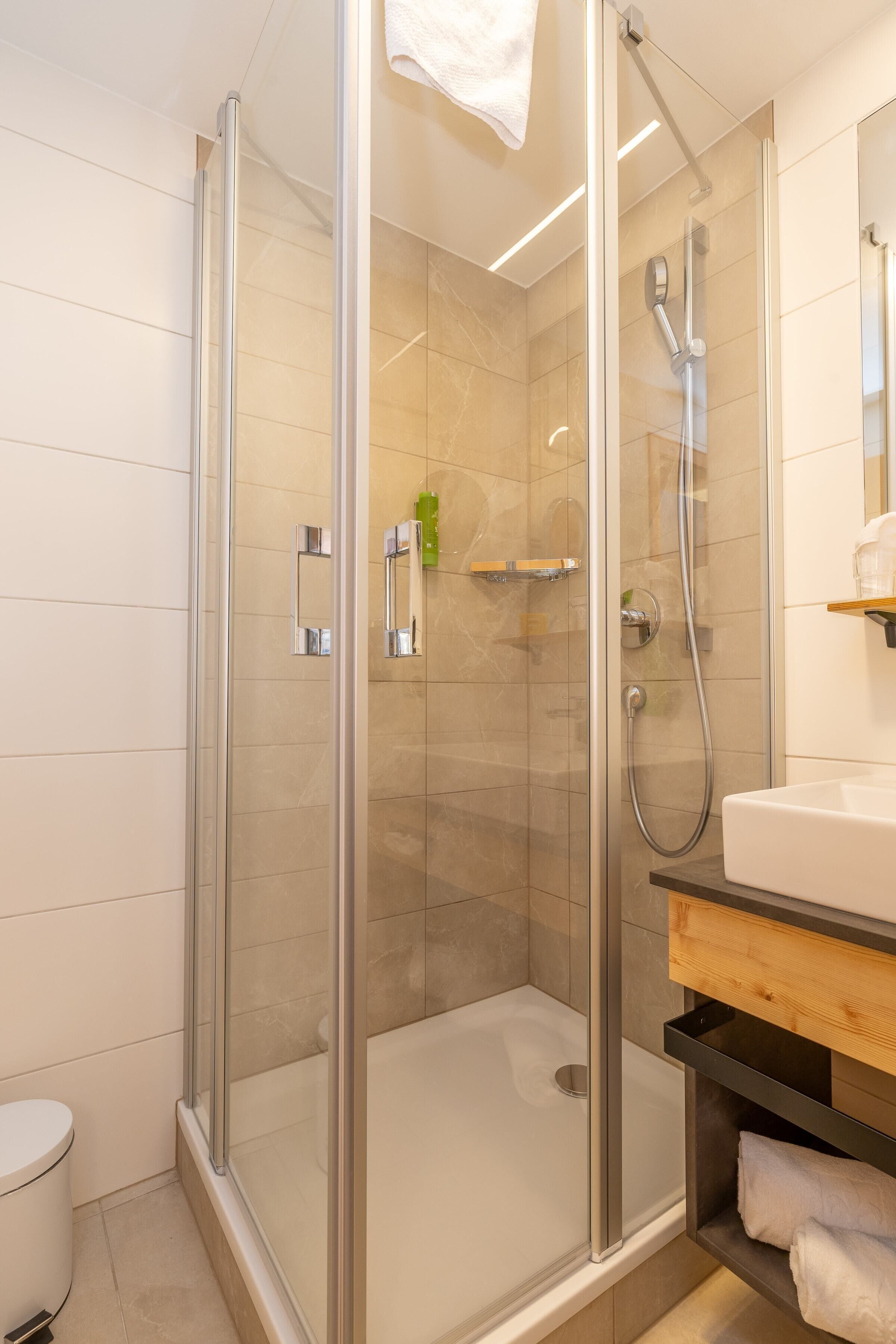 Ein modernes Badezimmer mit einer gläsernen Duschkabine, einem weißen Waschbecken und einer Holzwaschtischplatte.