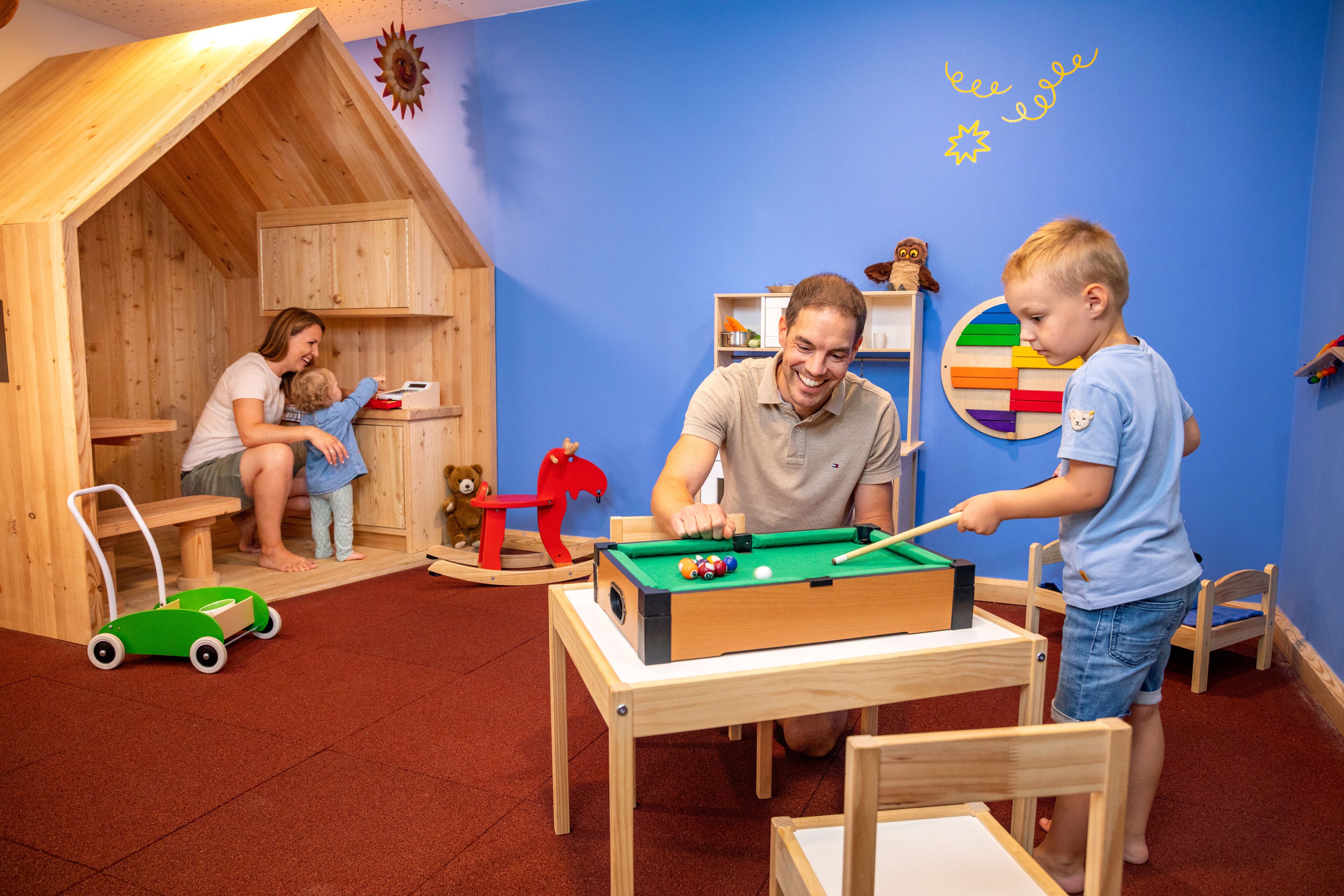 Un salón de juegos acogedor con mesa de billar, estructuras de madera para jugar y una pared azul con decoración de estrellas.
