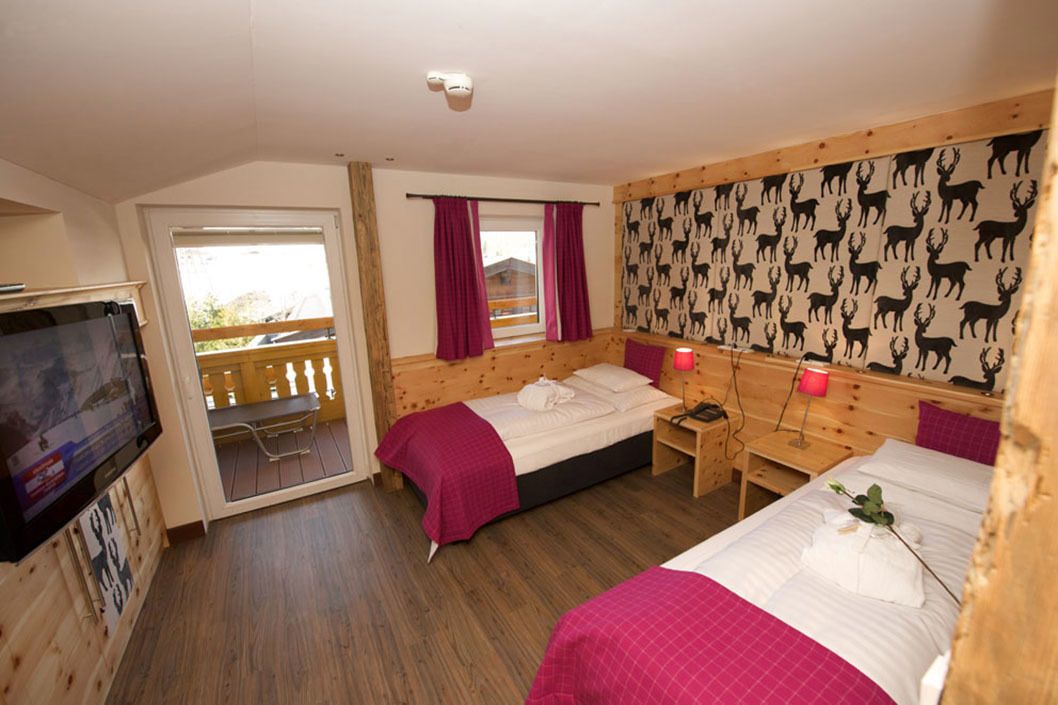 A room with two beds, a wooden headboard, a TV, and a balcony.