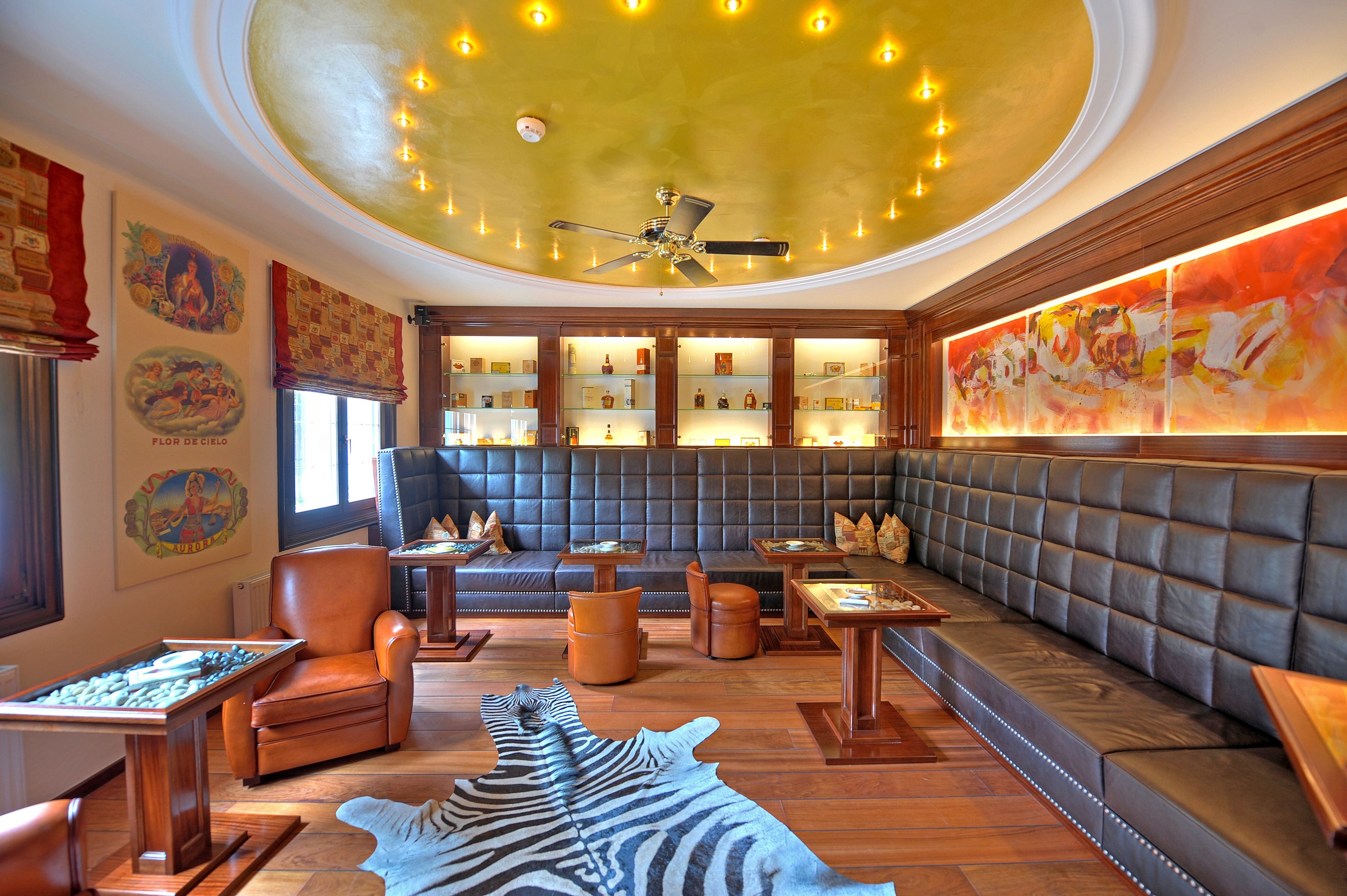 A luxurious lounge with leather seating, a ceiling fan, and a large abstract painting.
