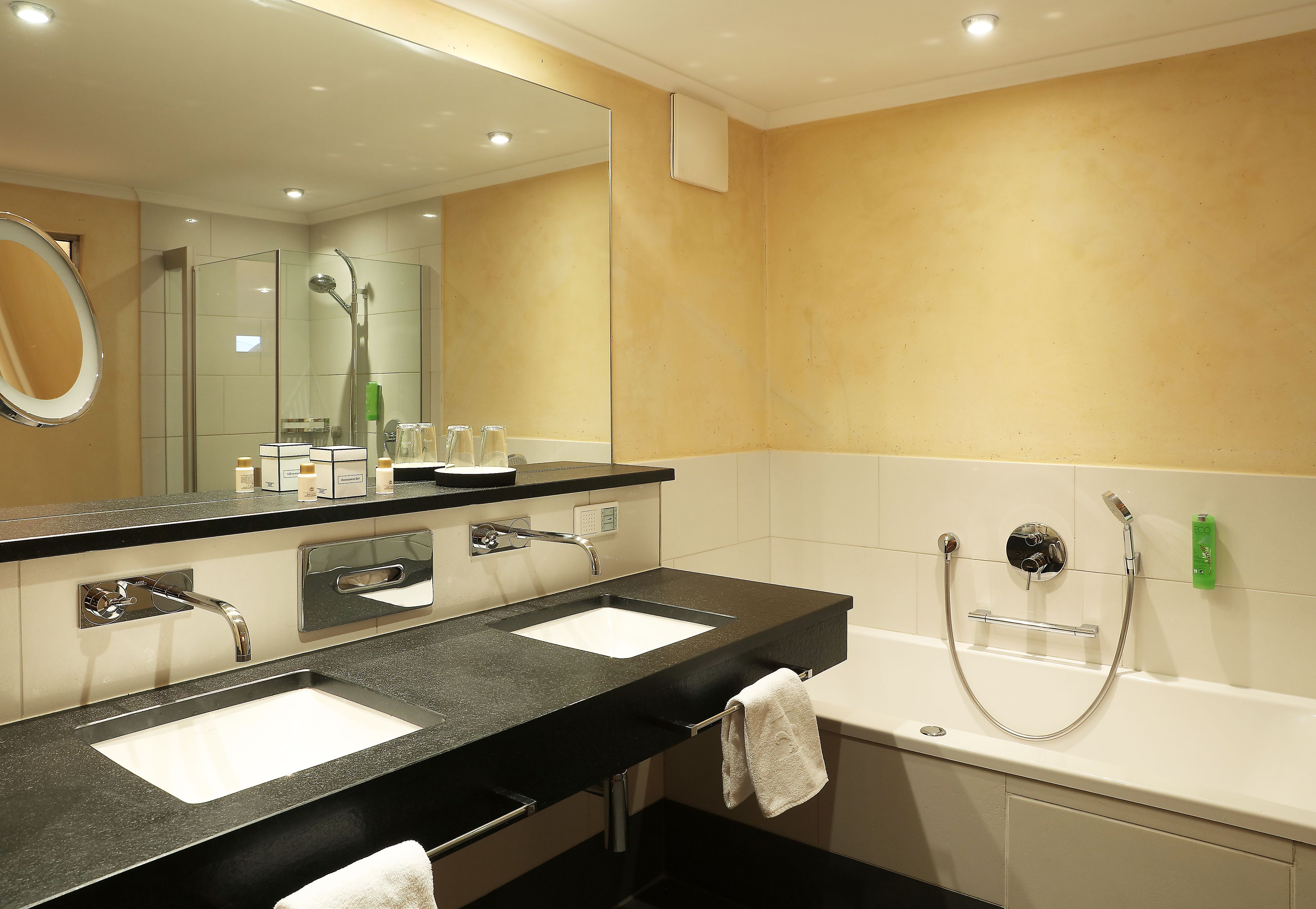 A modern bathroom with two sinks, a large mirror, and a bathtub.