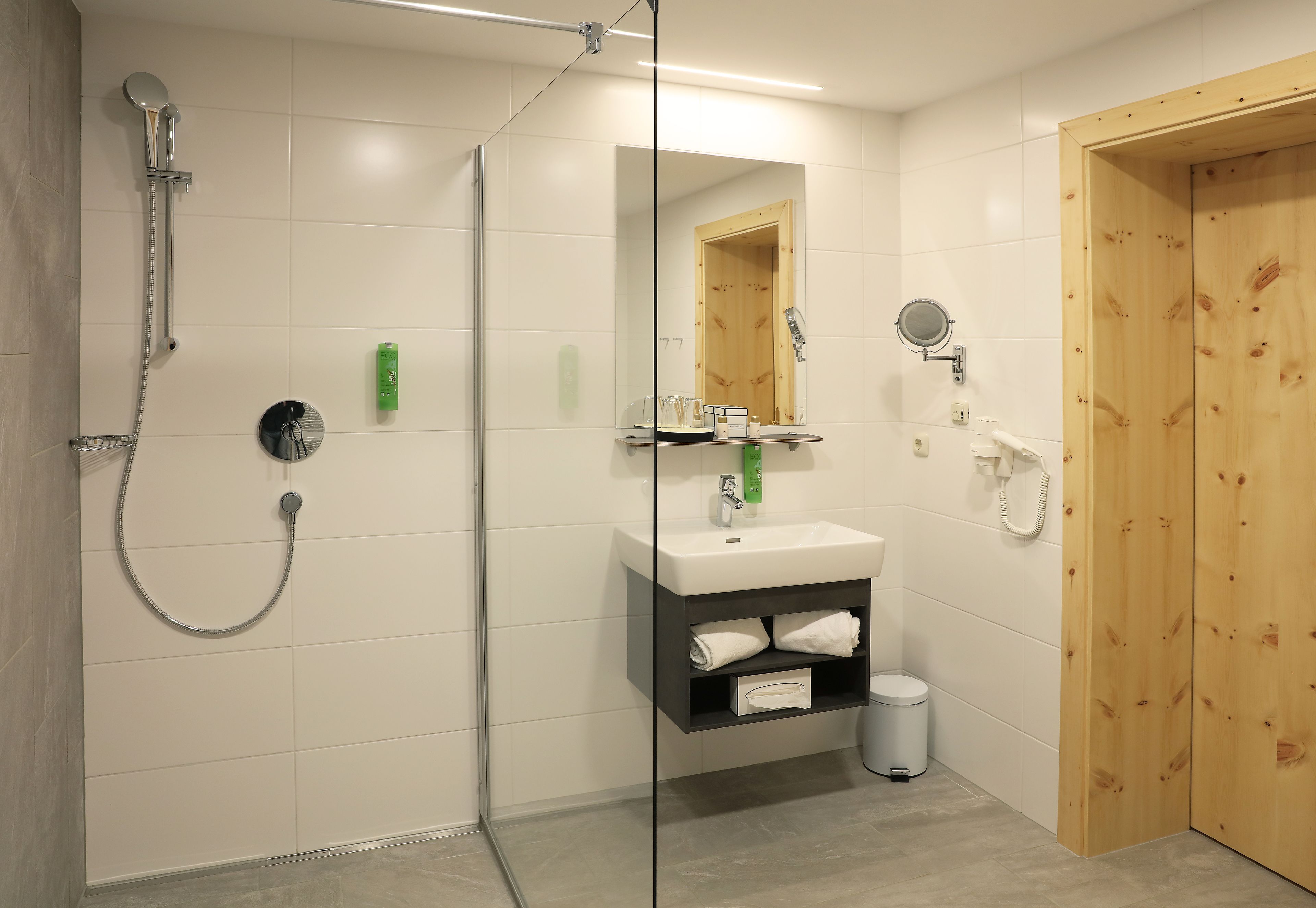 A modern bathroom with a glass-enclosed shower, a white sink with a mirror above it, and a wooden door.