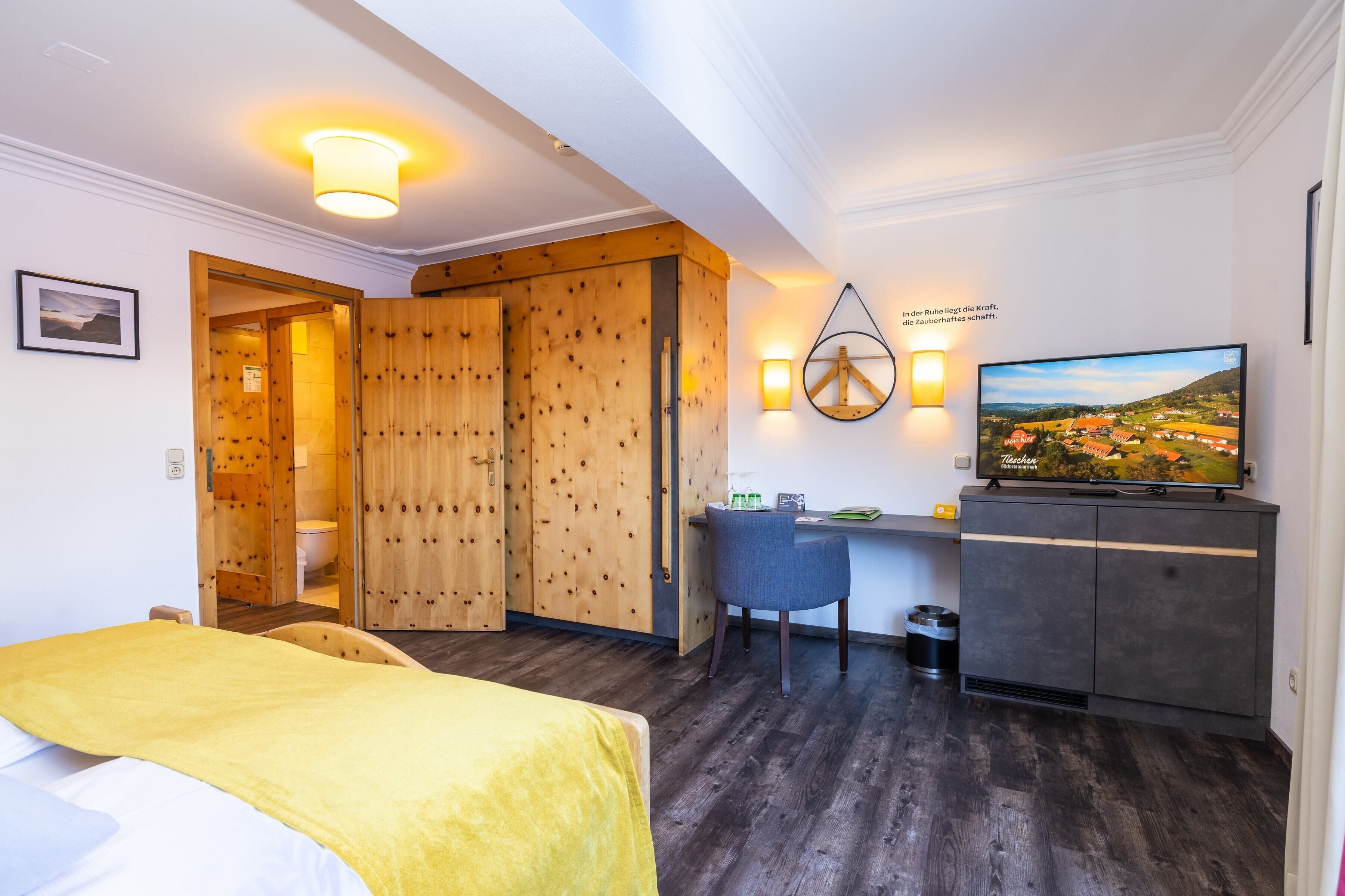 A hotel room with a bed, a desk, a chair, a television, and a wardrobe.