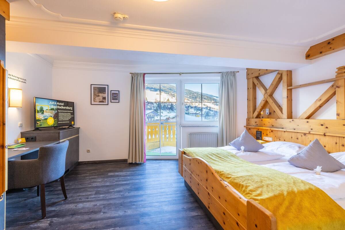 Et hotelværelse med en seng, et skrivebord, en stol og udsigt til et sneklædt landskab gennem et stort vindue.